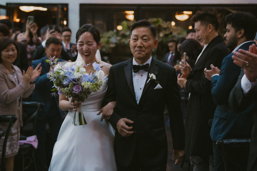 Bride smiling while walking down the aisle with her father