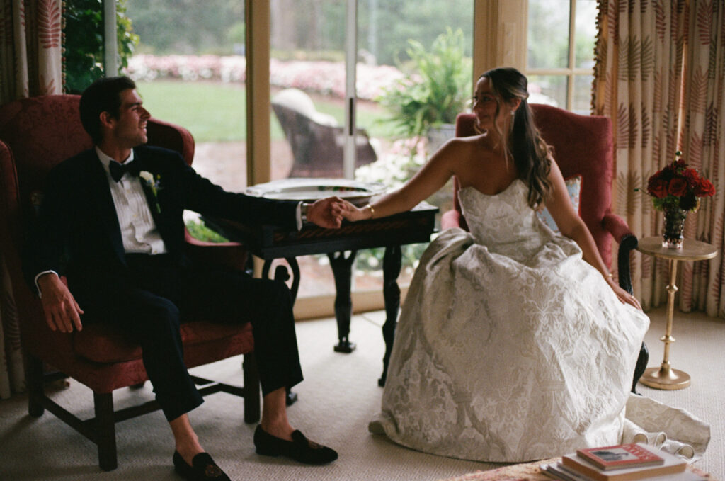 Bride and groom sitting down holding hands inside a historic estate wedding venue