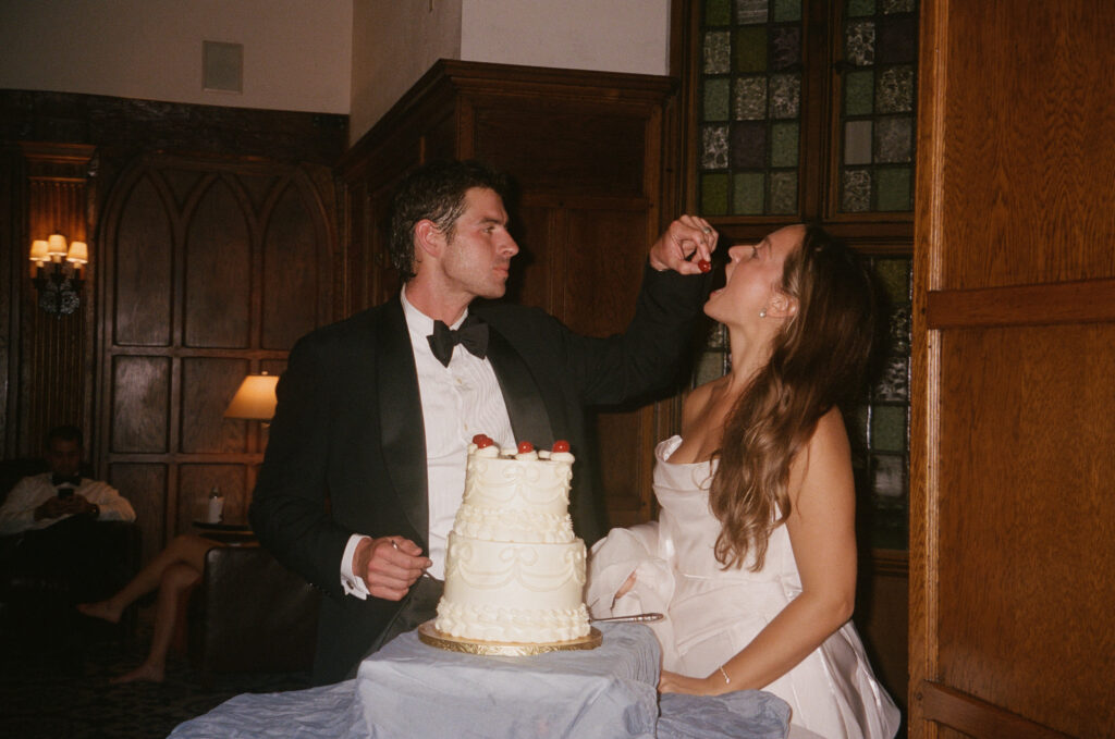 Groom feeding bride cherry from the top of wedding cake 