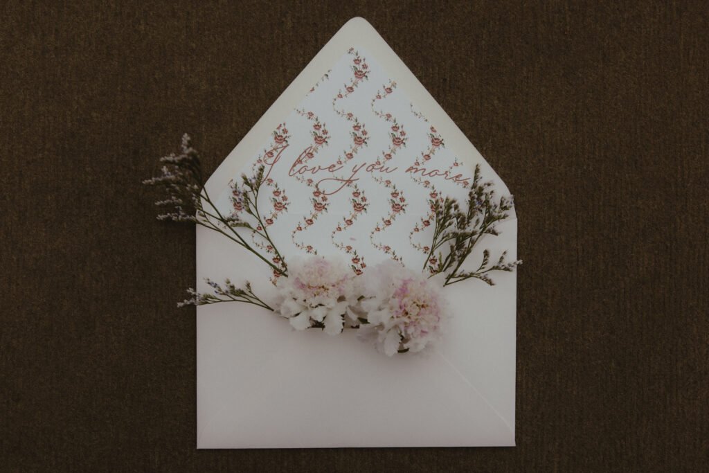 Flat Lay of Wedding Invitation Envelope with Flowers Sticking Out 