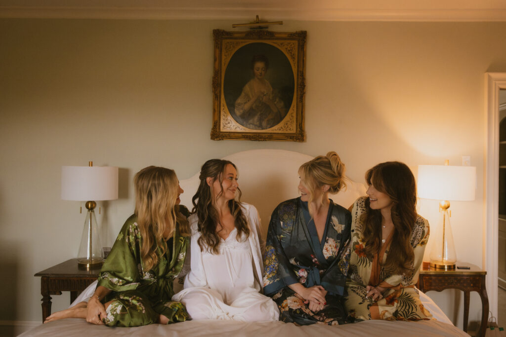 Bride and bridesmaids in robes sitting together and looking at each other during getting ready