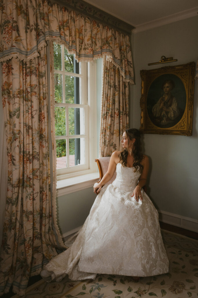 Bride in her wedding dress sitting in a chair looking out the window of a historic estate venue