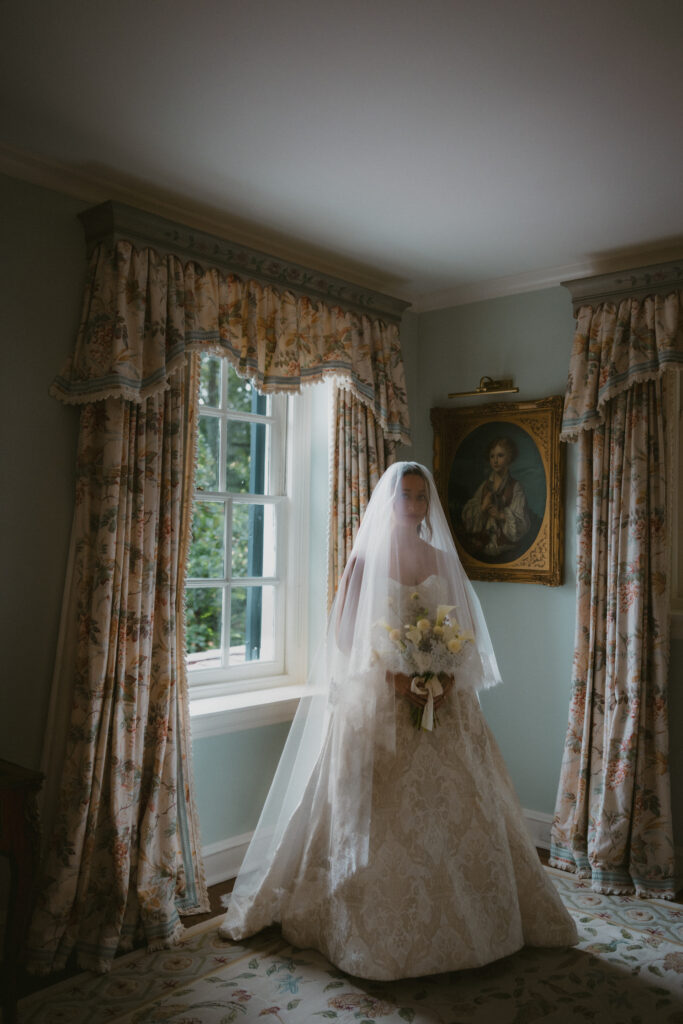Bride looking toward the camera while holding her bouquet with her veil covering her face 