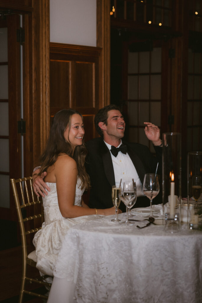 Bride and groom laughing at the sweetheart table during toasts