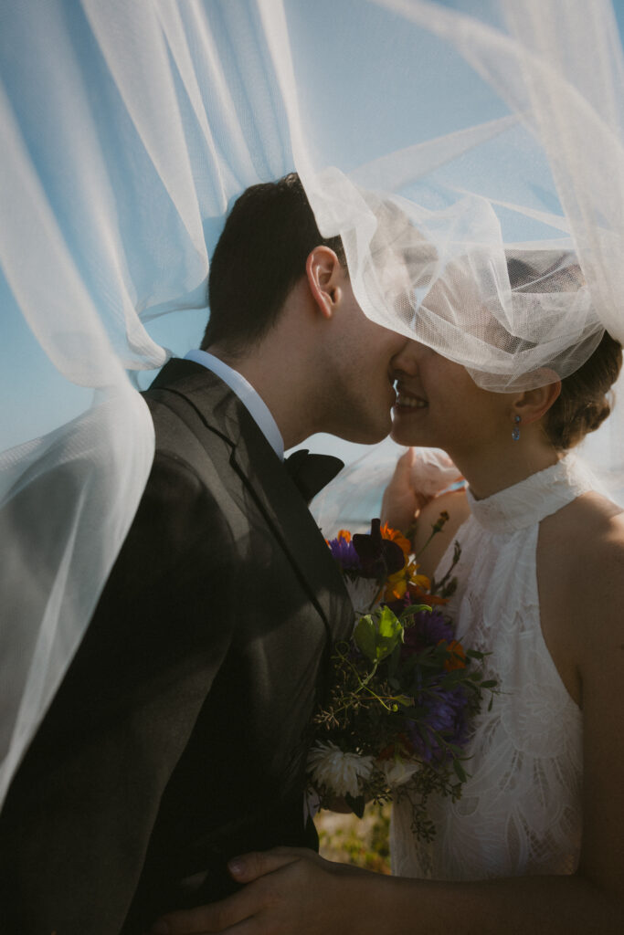 Bride and groom going in for a kiss with the veil flying in the air over them