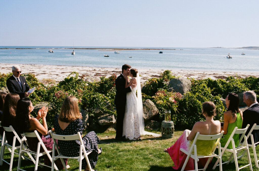 Bride and groom sharing their first kiss as a married couple with loved ones cheering around them