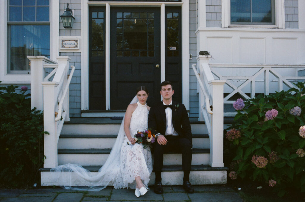 Bride and groom sitting on the steps of a classic New England beach house in Maine