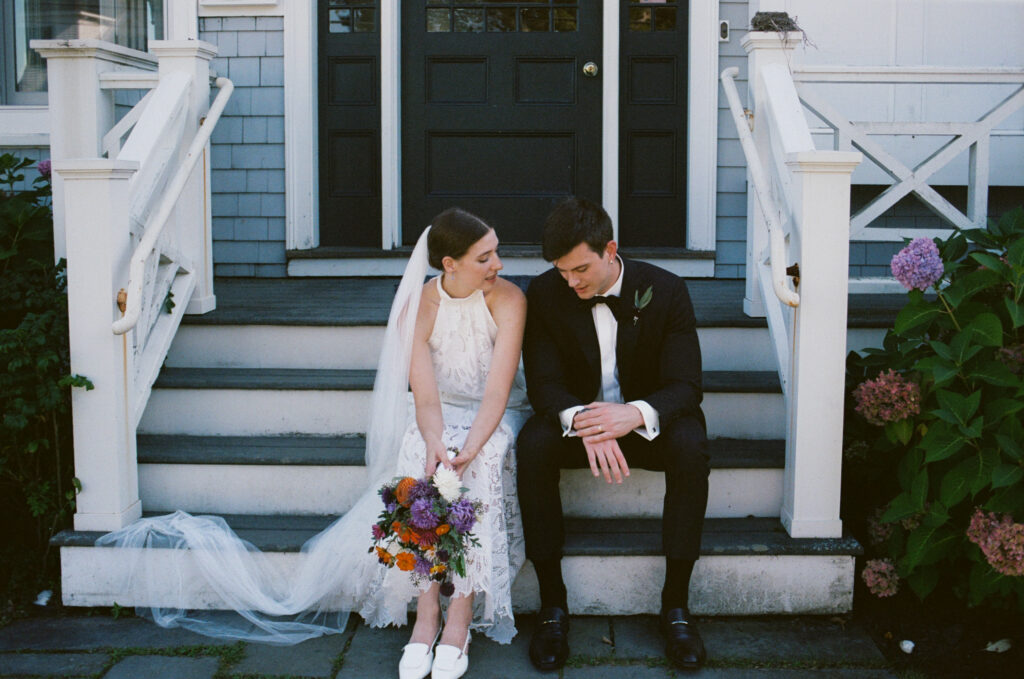 Bride and groom talking to each other while sitting on the steps of a classic New England beach house in Maine