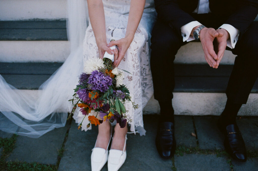 Close up image of the bride and groom's legs and bridal bouquet while sitting on the steps of a beach house