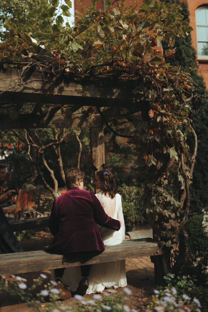 Brides sitting on a bench in a garden, taken from behind