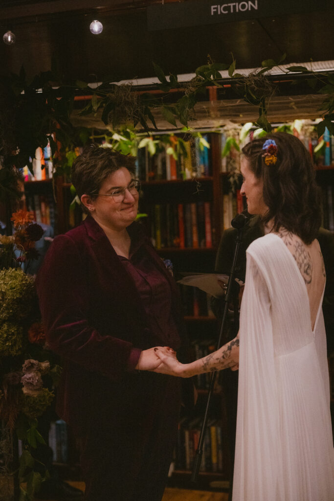 Brides holding hands and smiling during their wedding ceremony 