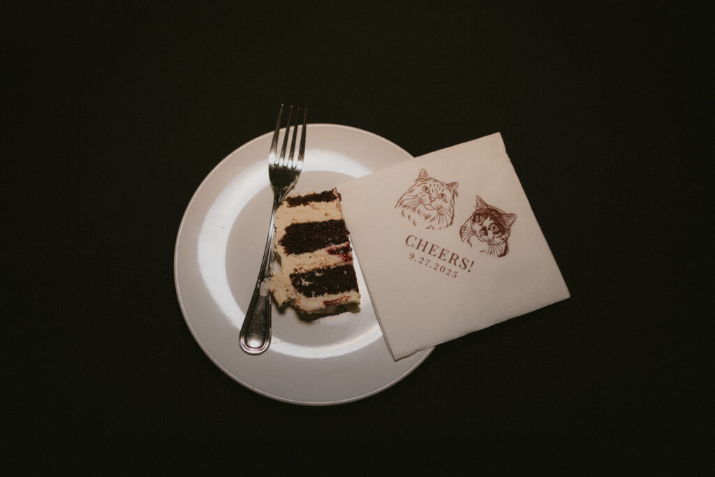 Detail shot of slice of cake and custom branded wedding napkins with the brides' cats on them 