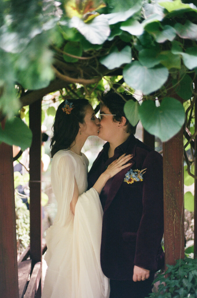 Brides kissing under a gazebo with plants framing the image