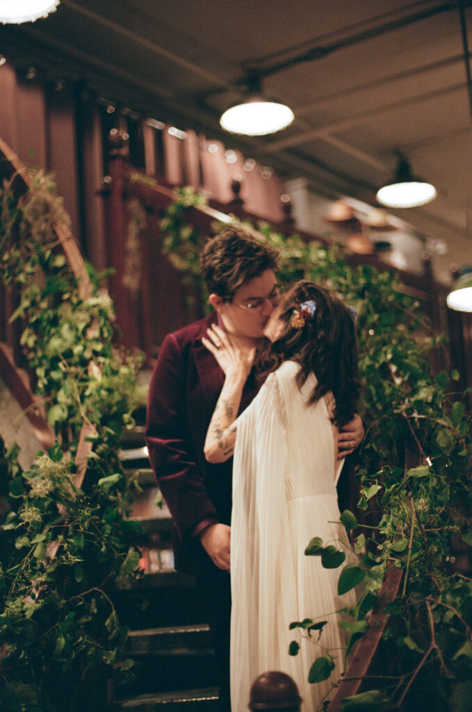 Film photo of brides kissing on the stairs in their housing works bookstore wedding venue 