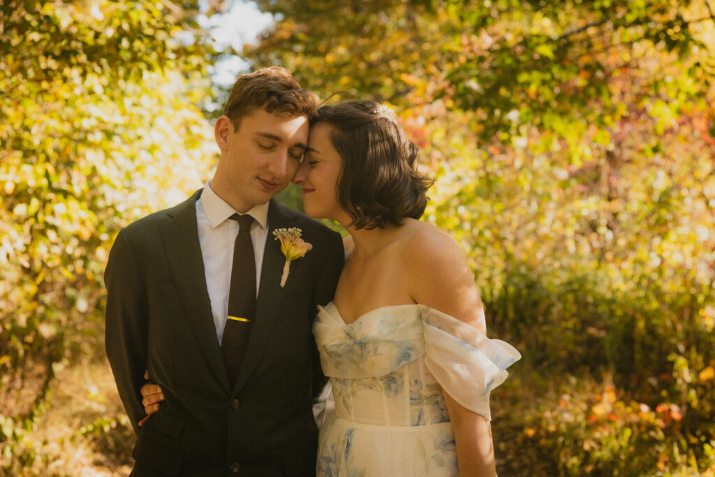 Bride and groom touching foreheads with fall foliage in the background