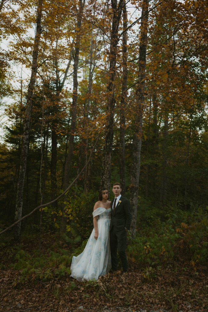 Bride and groom standing together in the woods surrounded by fall foliage