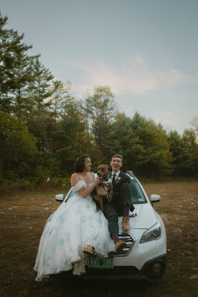 Bride and groom sitting on their car with their dog 