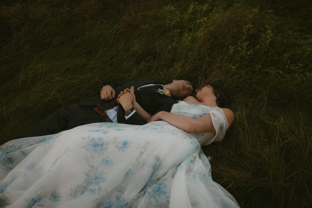 Bride and groom laying in a meadow looking into each other's eyes