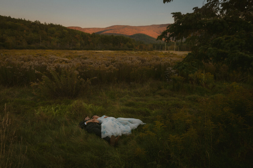 Bride and groom laying in a meadow with mountains in the background