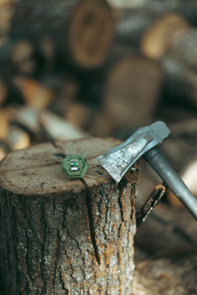 Rustic wedding ring detail shot on a log next to an axe 