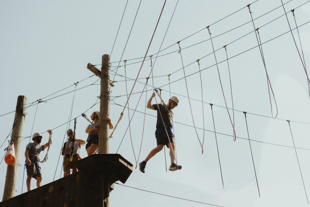 Groom tightrope walking toward a zip line at a summer camp wedding venue