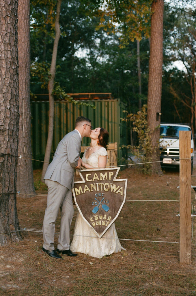 Bride and groom kissing next to the camp sign at a summer camp wedding venue