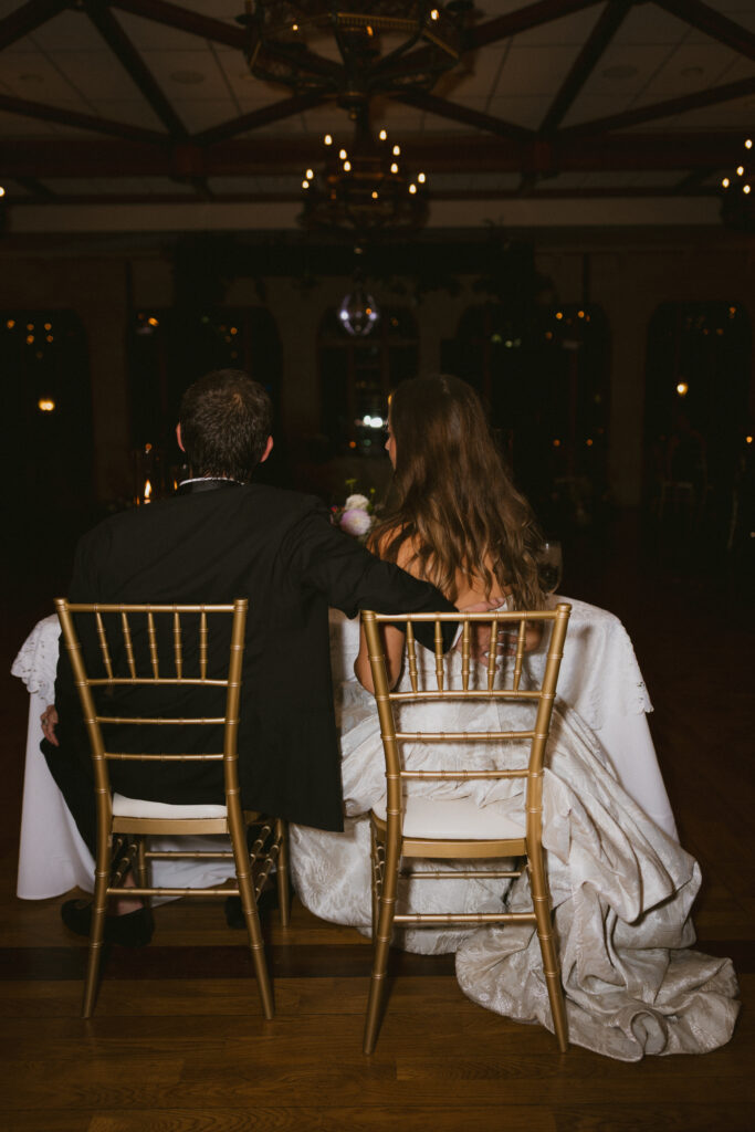 Bride and groom sitting at sweetheart table, taken from behind