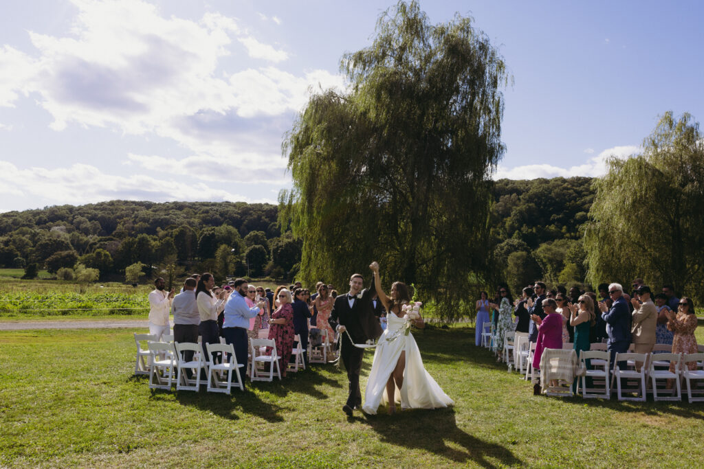 Bride and groom walking back down the aisle with their arms in the air 
