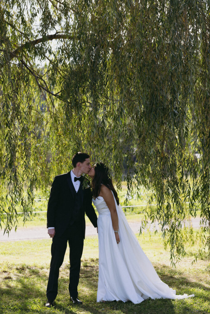 Bride and groom kissing each other under a willow tree
