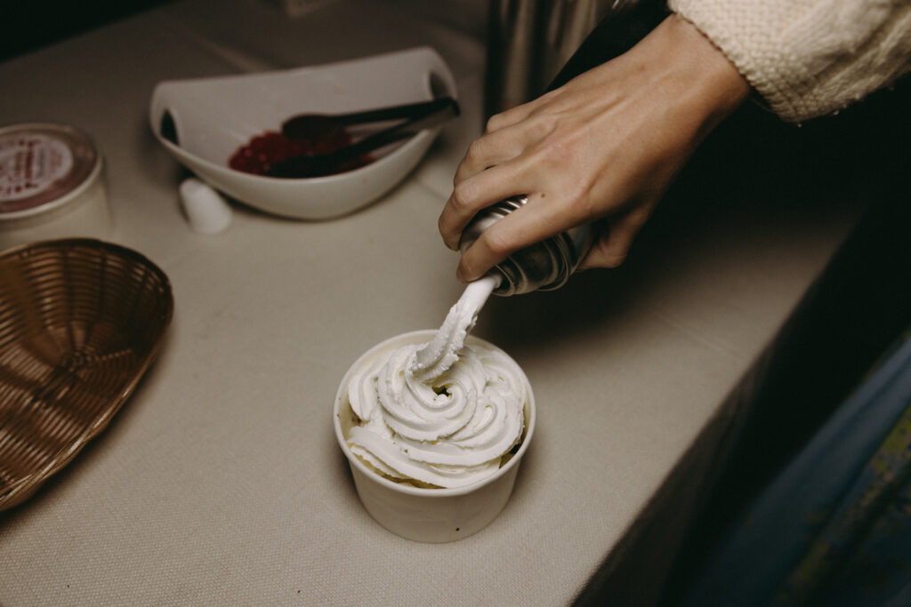 Close up shot of a guest putting whipped cream on a personal ice cream cup during a wedding reception
