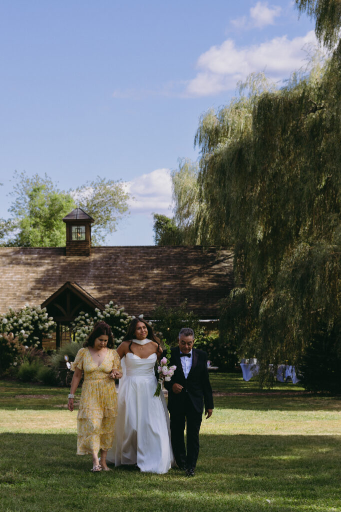 Bride walking down the aisle with both of her parents at a New England farm wedding