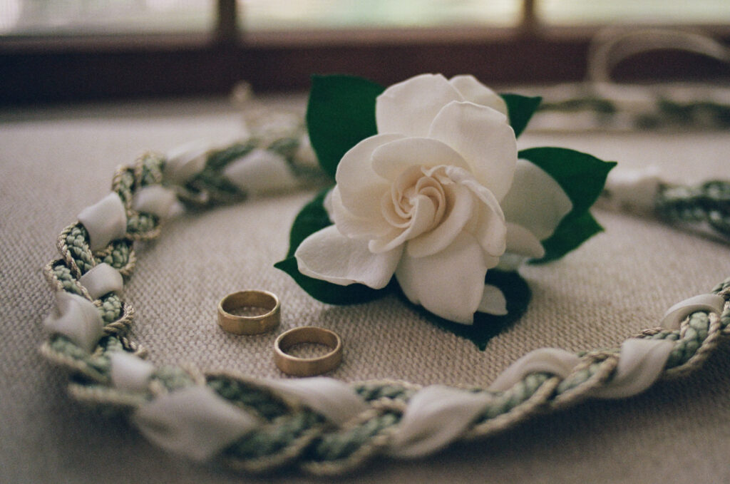Wedding rings, rose, and hand fasting cords detail image