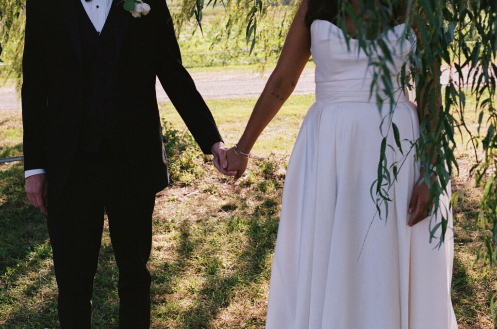 Close up image of bride and groom holding hands under a willow tree