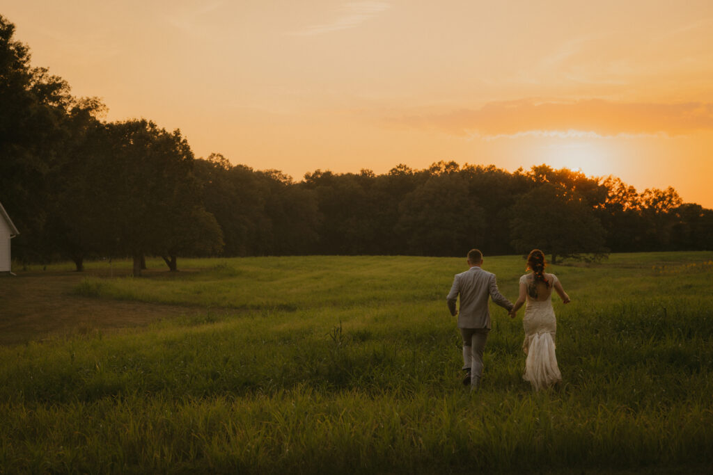Bride and groom running through a field at sunset