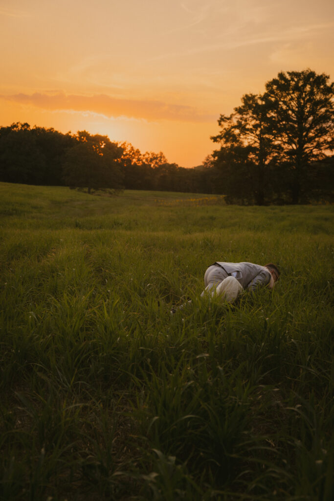 Bride and groom falling in a grassy field at sunset