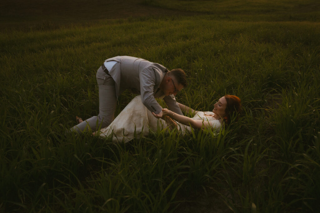 Bride and groom falling in a grassy field at sunset