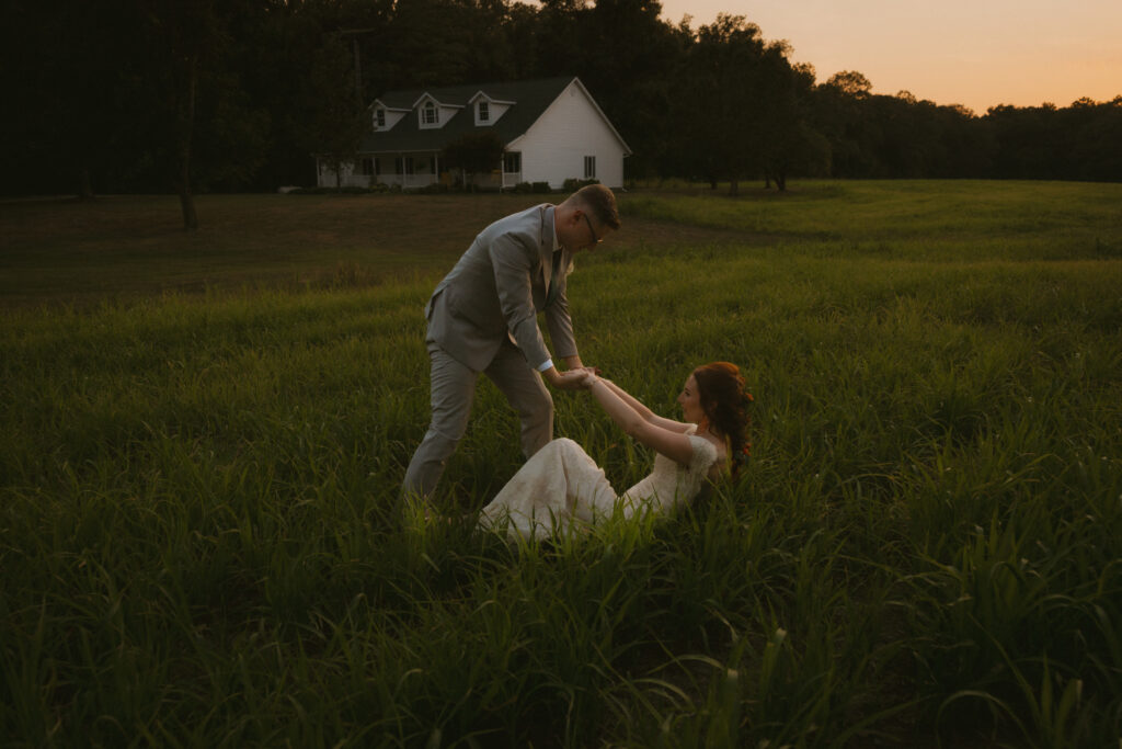 Bride and groom falling in a grassy field at sunset