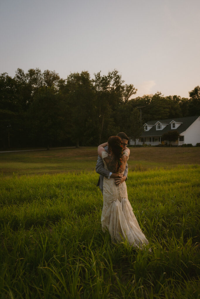 Bride and groom hugging in a grassy field at sunset