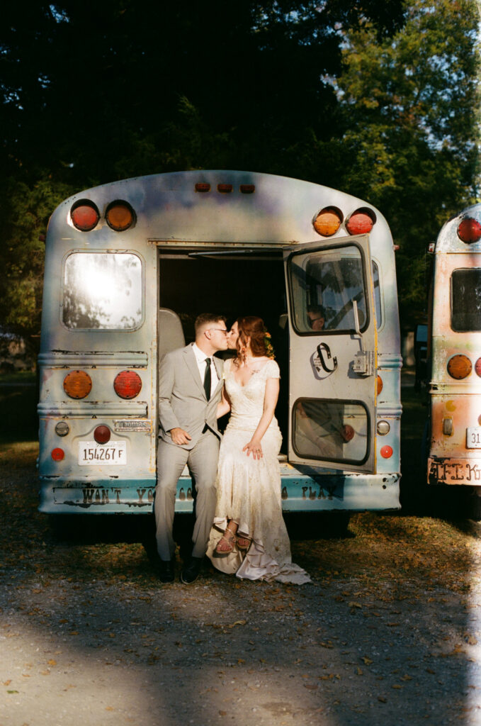 Bride and groom kissing in the back of a summer camp bus