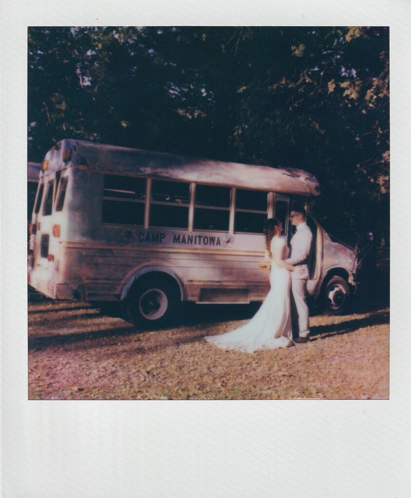 Bride and groom in front of a summer camp bus