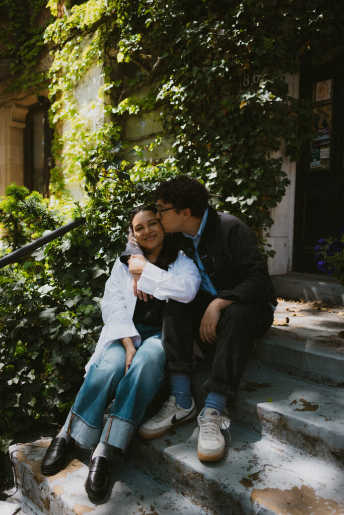 Engaged couple sitting on steps with their arms around each other smiling