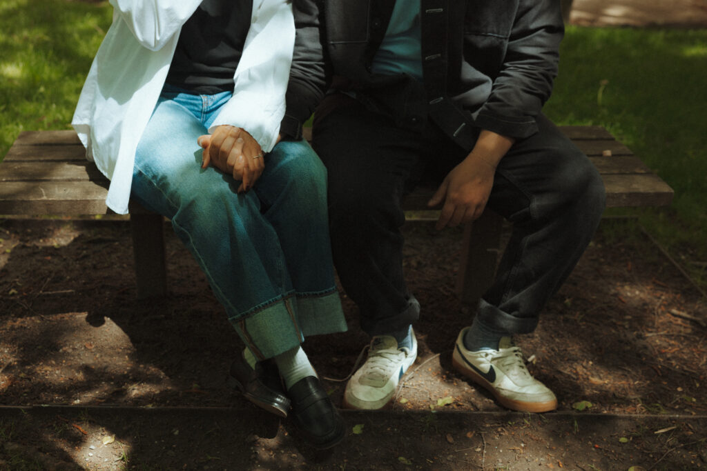 Close up of an engaged couple holding hands and sitting on a bench, from the chest down
