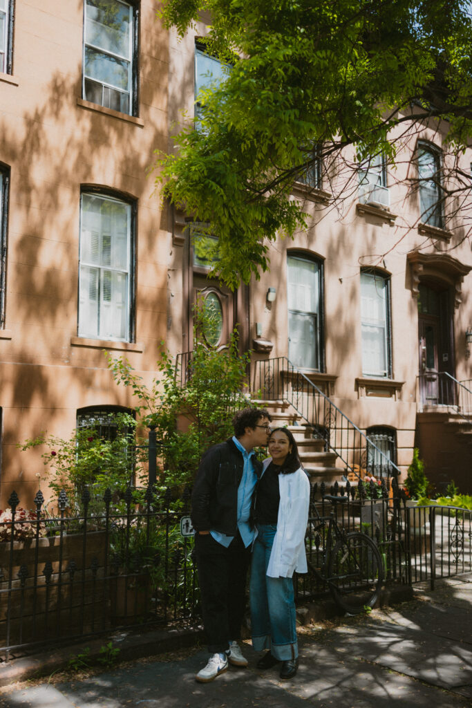 Engaged couple standing in front of a brownstone building in Brooklyn