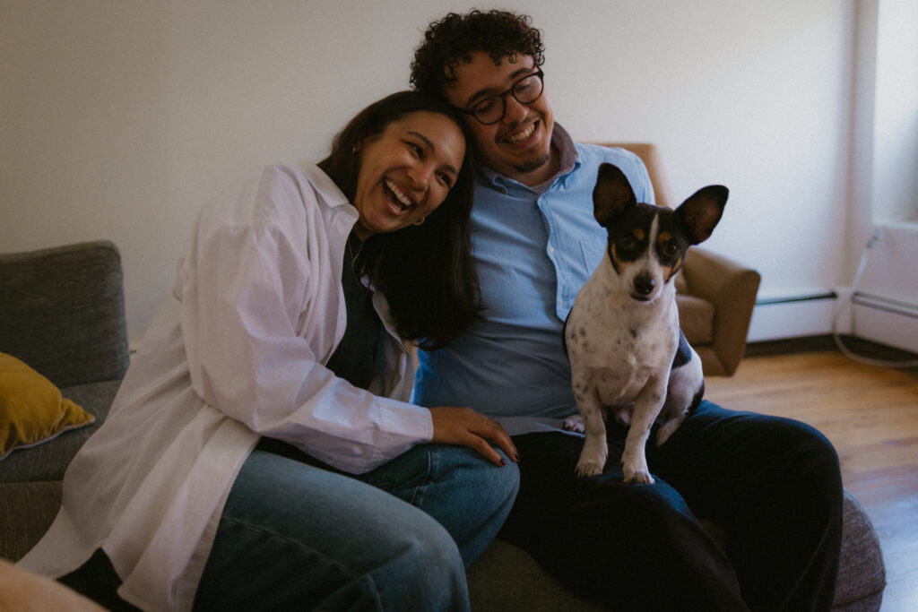 Engaged couple sitting and laughing with their dog in their lap