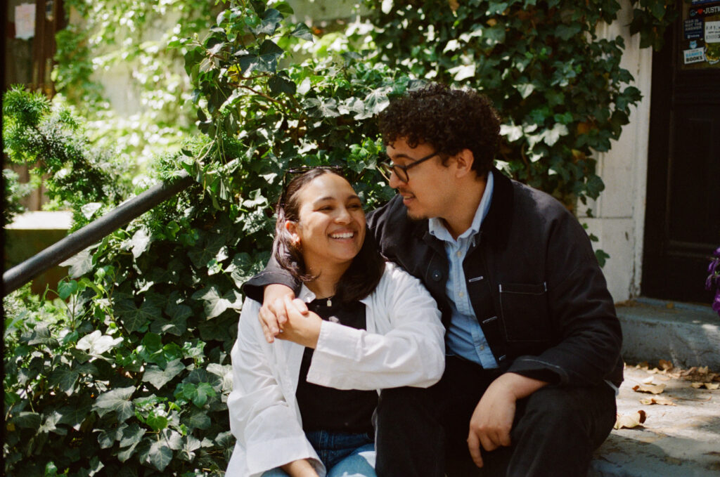 Engaged couple sitting on steps with their arms around each other smiling
