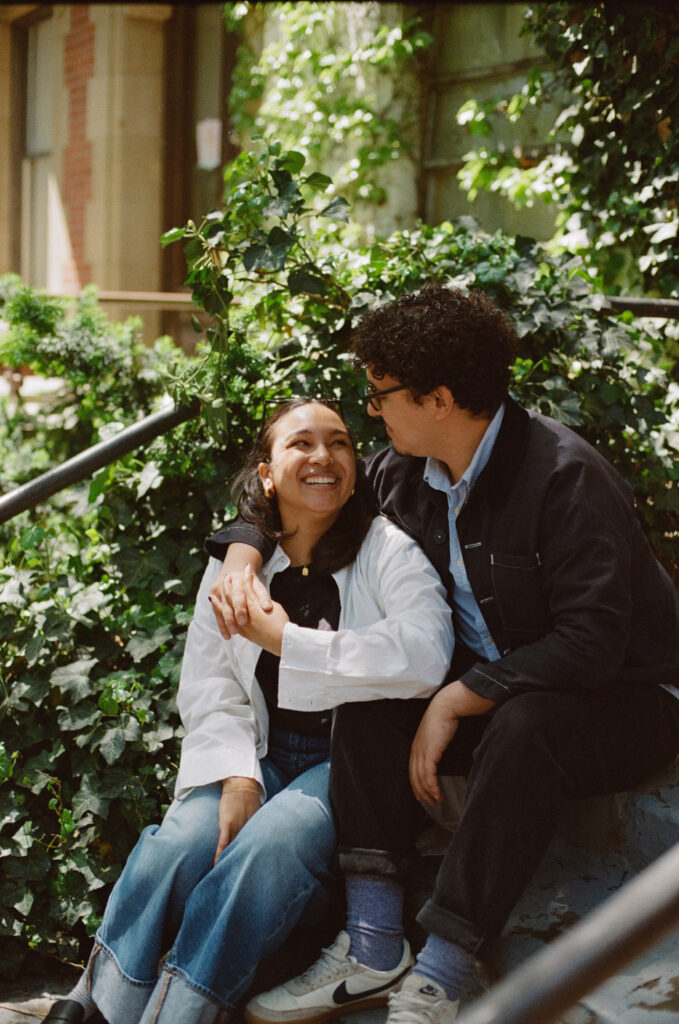 Engaged couple sitting on steps with their arms around each other smiling