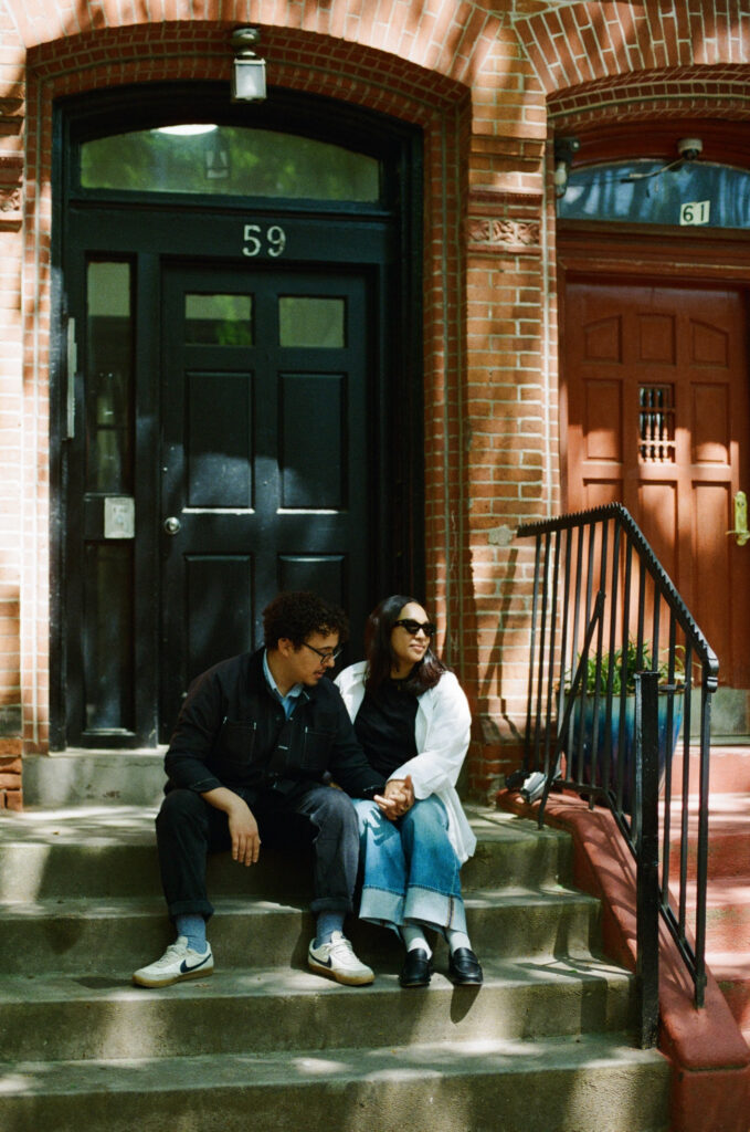 Engaged couple sitting on the steps of a brownstone building in Brooklyn