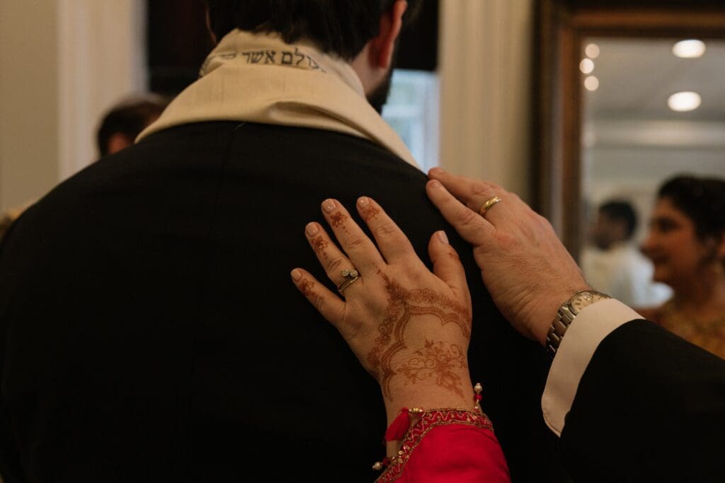 Groom's parents hands on the groom's shoulder during the Ketubah signing