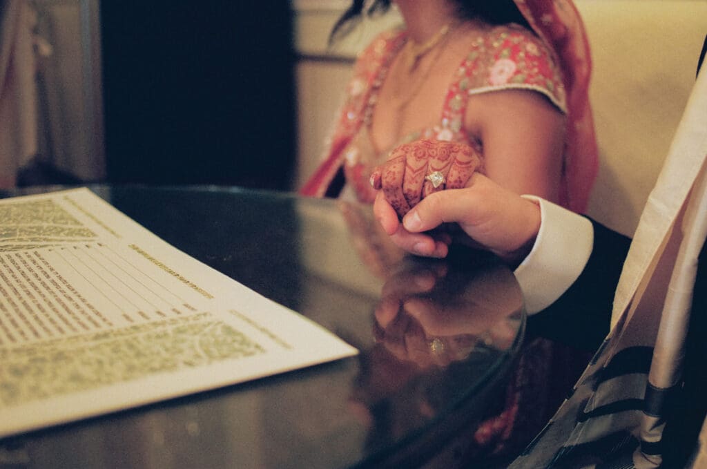 Close up of the bride and groom holding hands during the Ketubah signing