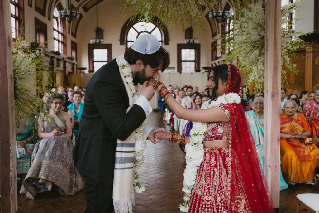 Groom kissing the bride's hand after exchanging garlands